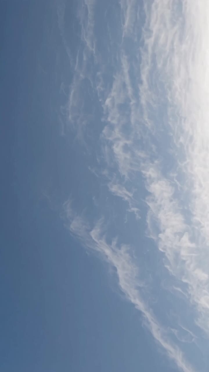 A serene video captures wispy clouds against a clear blue sky from a low-angle perspective
