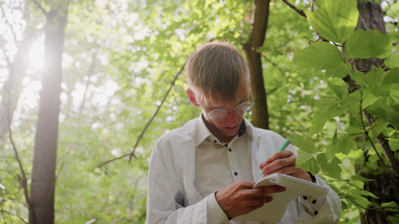 Biologist in white coat stands in forest under bright sunlight with serious expression writing notes in jotter using pen, documenting ecological research observations surrounded by lush green leaves