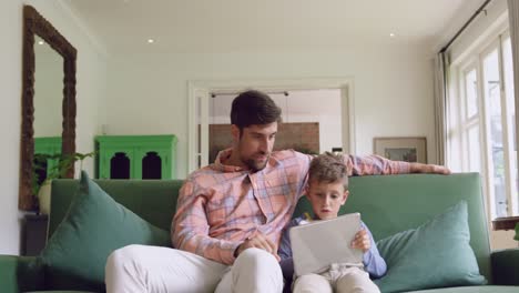 Father-and-son-using-digital-tablet-on-sofa-at-home-4k