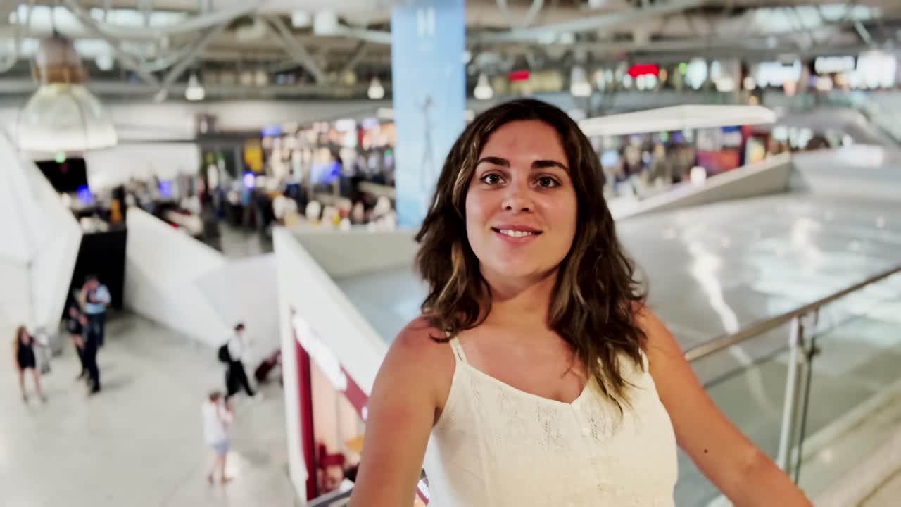 Donna sulla scala mobile in aeroporto, sorride luminosamente alla telecamera