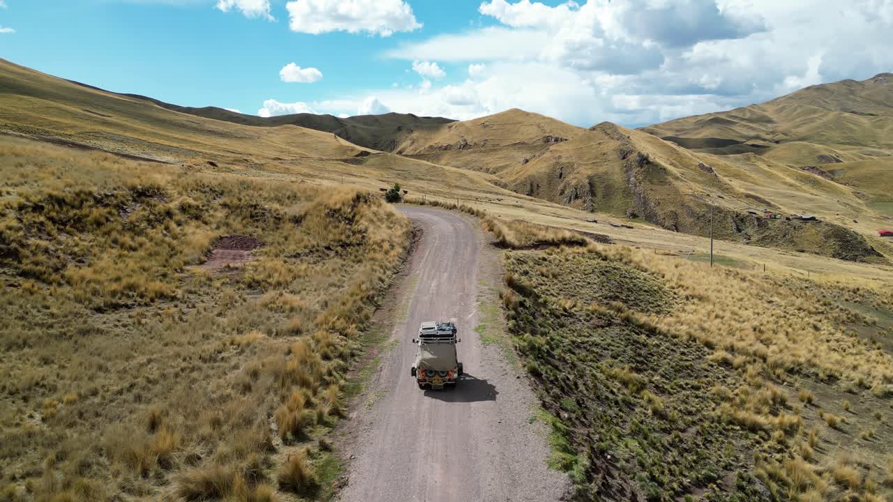 Drone footage capturing a tuk tuk journey through soft, windswept grass in a highland valley, framed by distant mountain peaks