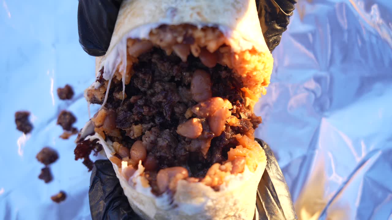 Gros plan sur un burrito fraîchement préparé, ouvert par deux mains, révélant une garniture savoureuse de viande et de légumes. Met en avant la fraîcheur, la texture et l’attrait de la cuisine de rue mexicaine.