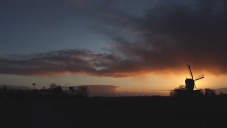 Traffic-driving-past-old-windmill-at-sunset-in-the-Netherlands