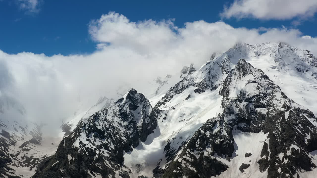 Volo aereo tra le nuvole di montagna sopra splendide vette innevate e ghiacciai.