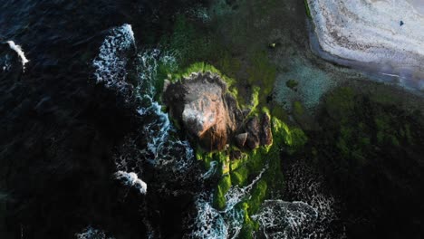 arc aerial shot around rock in the sea at sunset, bright colors and dark water