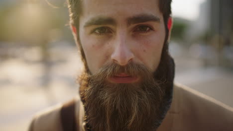 close up portrait of pensive young bearded hipster man looking serious intense at camera staring urban background