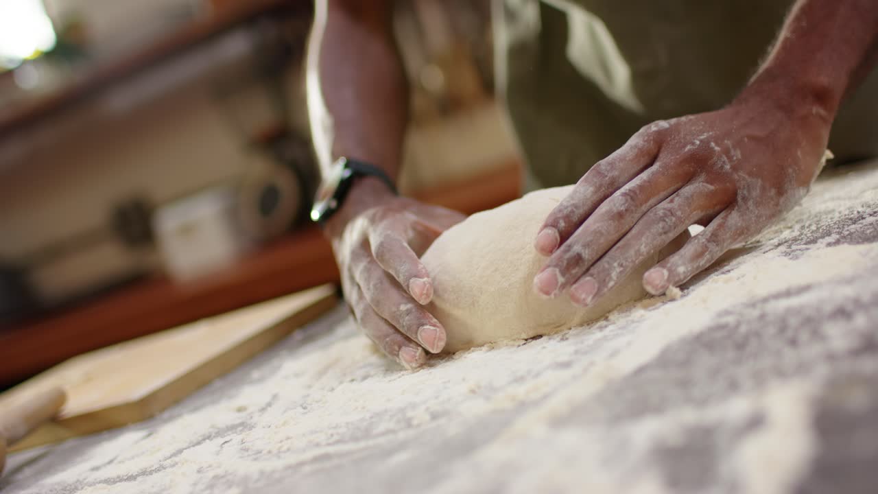 Man in green apron floured hands shaping dough on floured board pressing, folding for baking