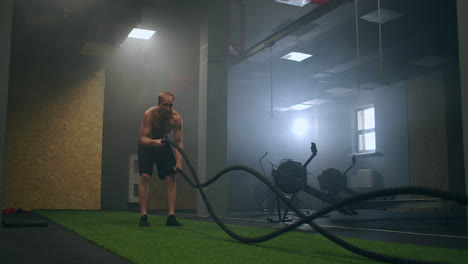 Fitness-man-exercising-with-battle-rope-abandoned-warehouse.-Tough-man-working-out-in-cross-training-gym-made-inside-old-factory.