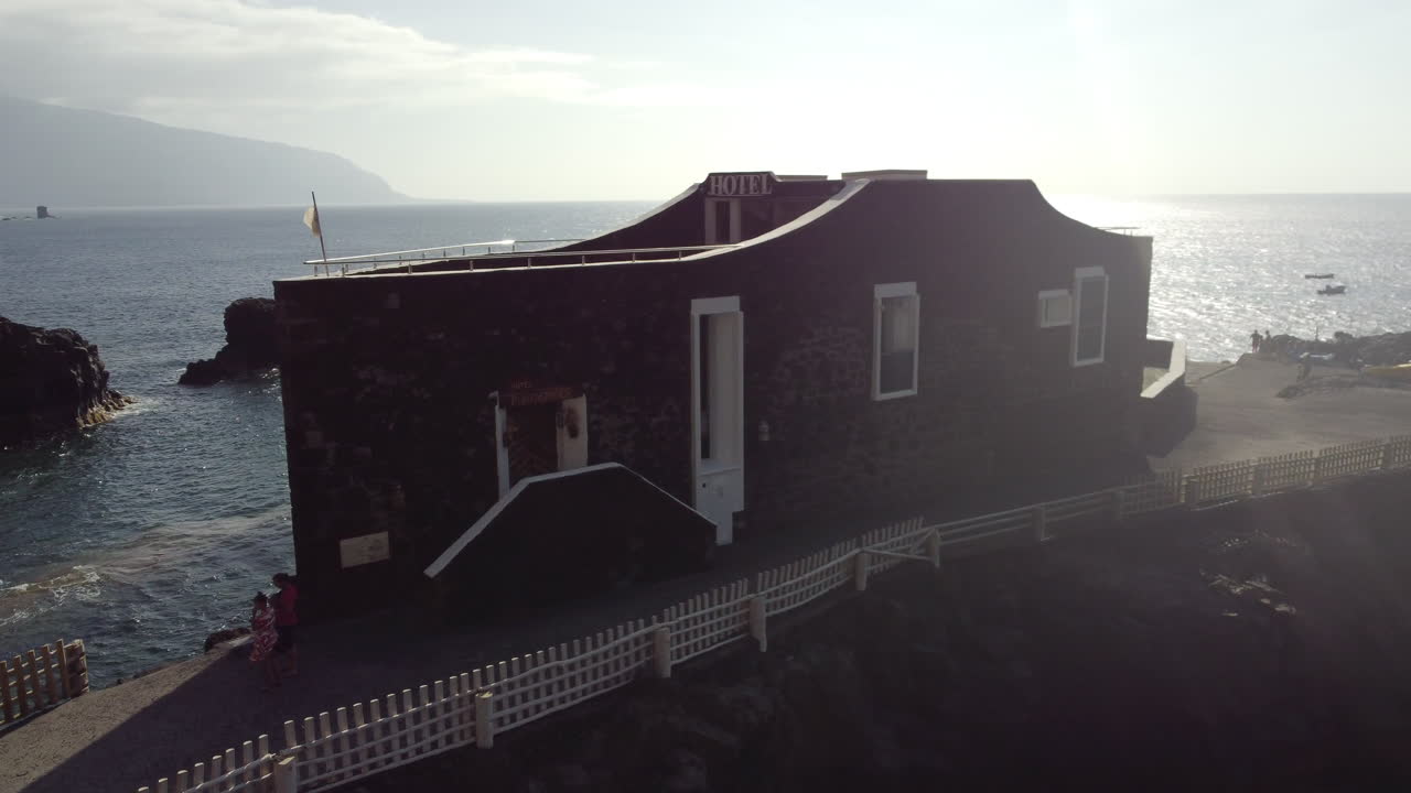 View of the Mirador de la Peña viewpoint surrounded by a white fence on a rocky mountain on a sunny windy day with tourist visitors, El Golfo, Hierro Island