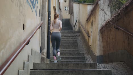 slim caucasian woman running and jogging upstairs at an urban city alley stairs, still shot seen from behind