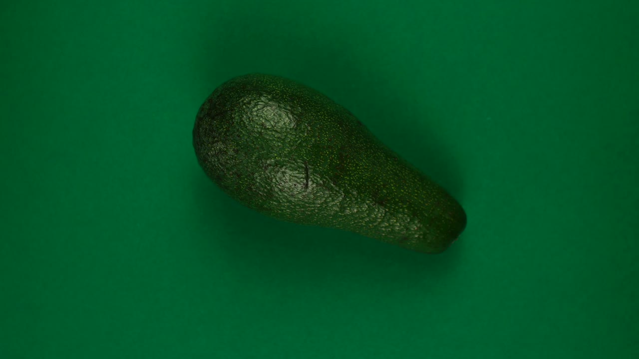 전체 아보카도 과일은 초록색 배경에서 빠르게 회전하고 있습니다.