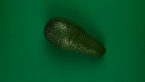 whole avocado fruit is rotating fast on green background.
