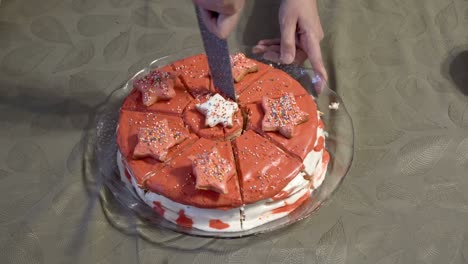 una mujer corta una decoración de estrellas de la mitad de un hermoso pastel con un gran cuchillo de cocina. el pastel casero está decorado con crema, chocolate rojo y estrellas. primer plano. sin rostro. vista superior. 4k.