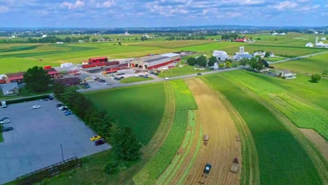 An-Aerial-Traveling-View-of-Corn-Fields-and-Harvesting-Crops,-With-a-Train-Yard-and-Patches-of-Color-on-a-Beautiful-Summer-Day