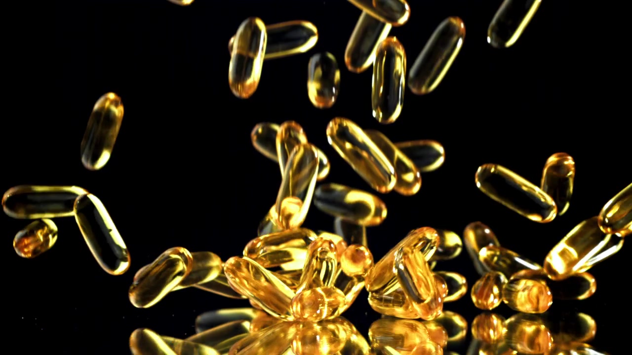 Capsule dorate di Omega-3 che cadono e rimbalzano su una superficie nera riflettente