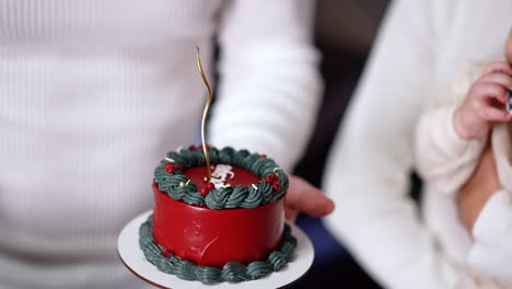 unrecognized man holds a little red cake near the baby. man lights the thin curved candle on the cake. close up.