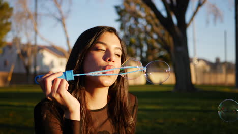 linda mujer hispana soplando burbujas mientras sonríe y se ve feliz y nostálgica al aire libre a la luz del sol
