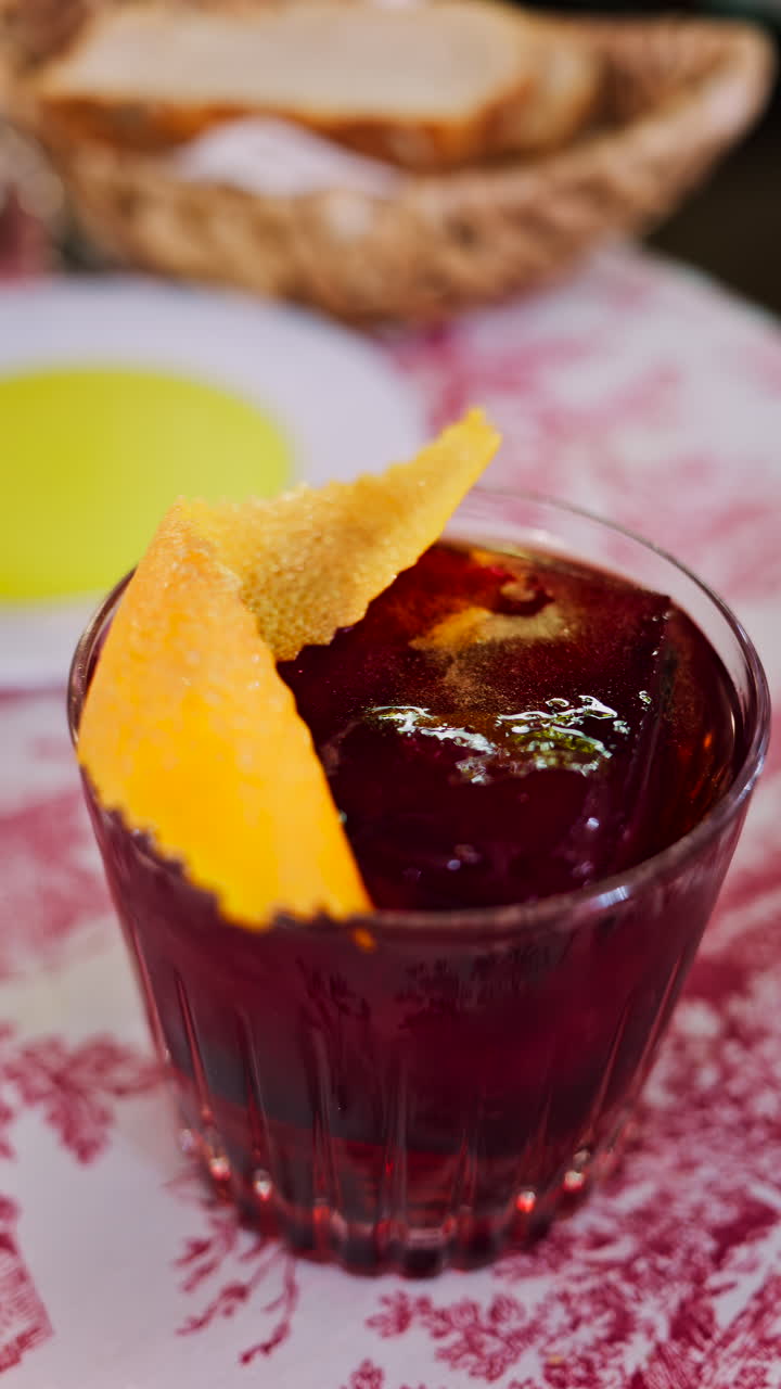 Close up of a negroni cocktail on a red and white tablecloth at a restaurant. Vertical