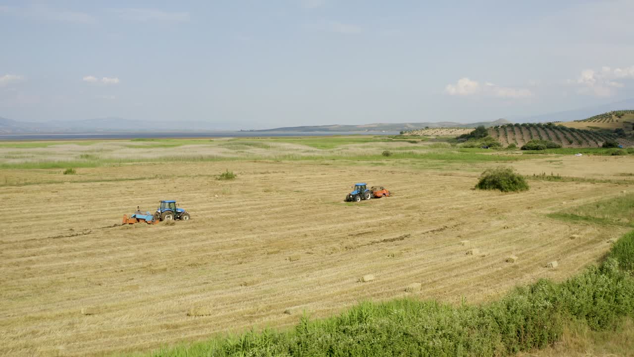 Flyfoto av en bonde på en traktor med en full tilhenger med halmballer.