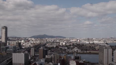 Wide-of-Japanese-Cityscape,-Kokura,-Kitakyushu,-Japan-with-Shinkanzen-Bullet-Train,-Mountains-and-River