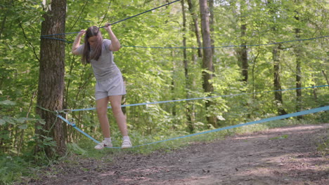 small girl in climbing equipment in a rope park. group of caucasian children training at boot camp. in the children camp children are taught to overcome obstacles with the help of a rope crossing