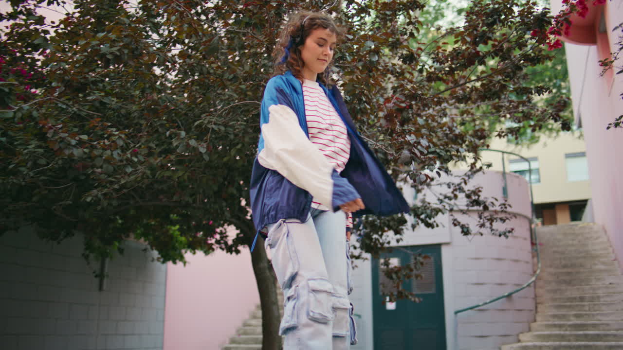 mujer de los años 90 escuchando música en auriculares en la calle con árboles en flor. niña bailando