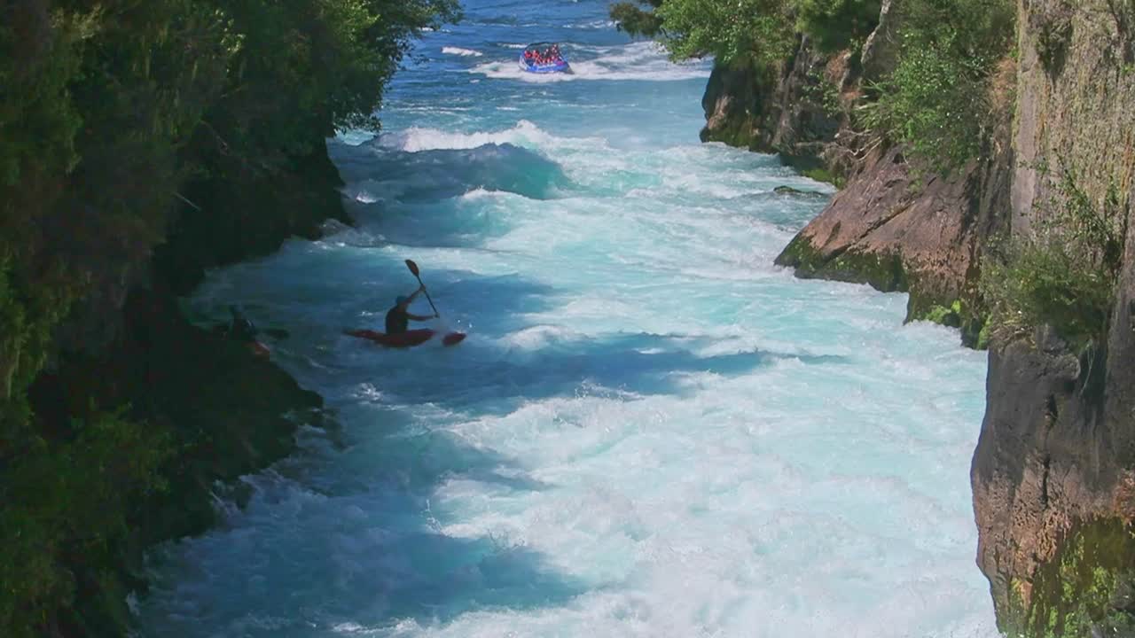 Tourist boat spins then a kayaker paddles down and over the Huka Falls at Taupo on the North Island of New Zealand
