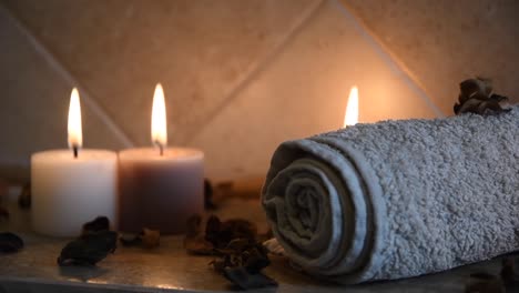 Relajante-Fondo-De-Spa-Con-Velas-Con-Llamas-Parpadeantes,-Algunos-Pétalos-De-Madera-Y-Una-Toalla