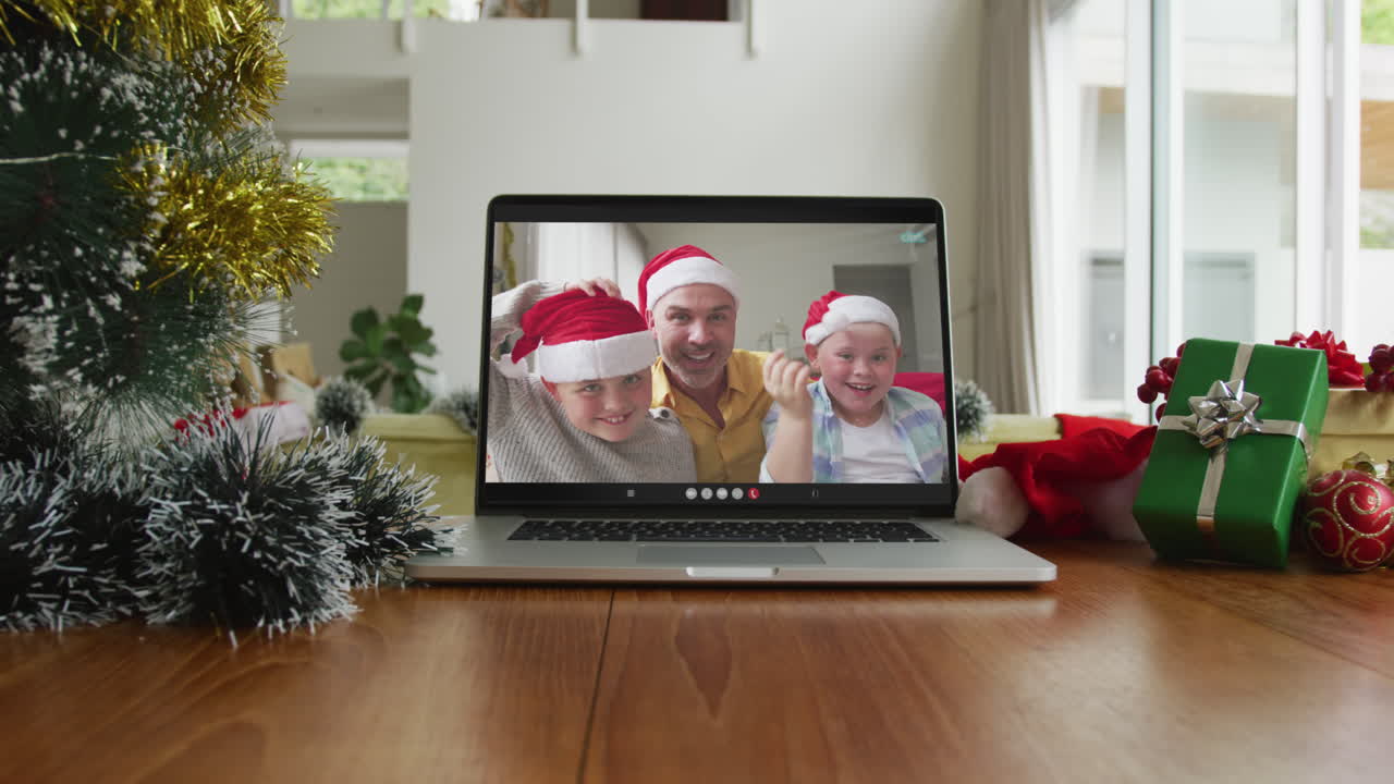 hombre caucásico sonriente con dos hijos que usan sombreros de santa claus en una videollamada de navidad en una computadora portátil