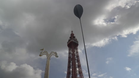 Blackpool-Tower,-artisanal-lamp-post-with-seagulls-and-tall-swaying-seed-structure-with-clouds-moving-in-different-directions