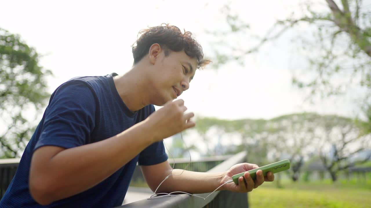 4k 아시아 남자가 아침에 공원에서 조하는 동안 음악을 듣고 있습니다.