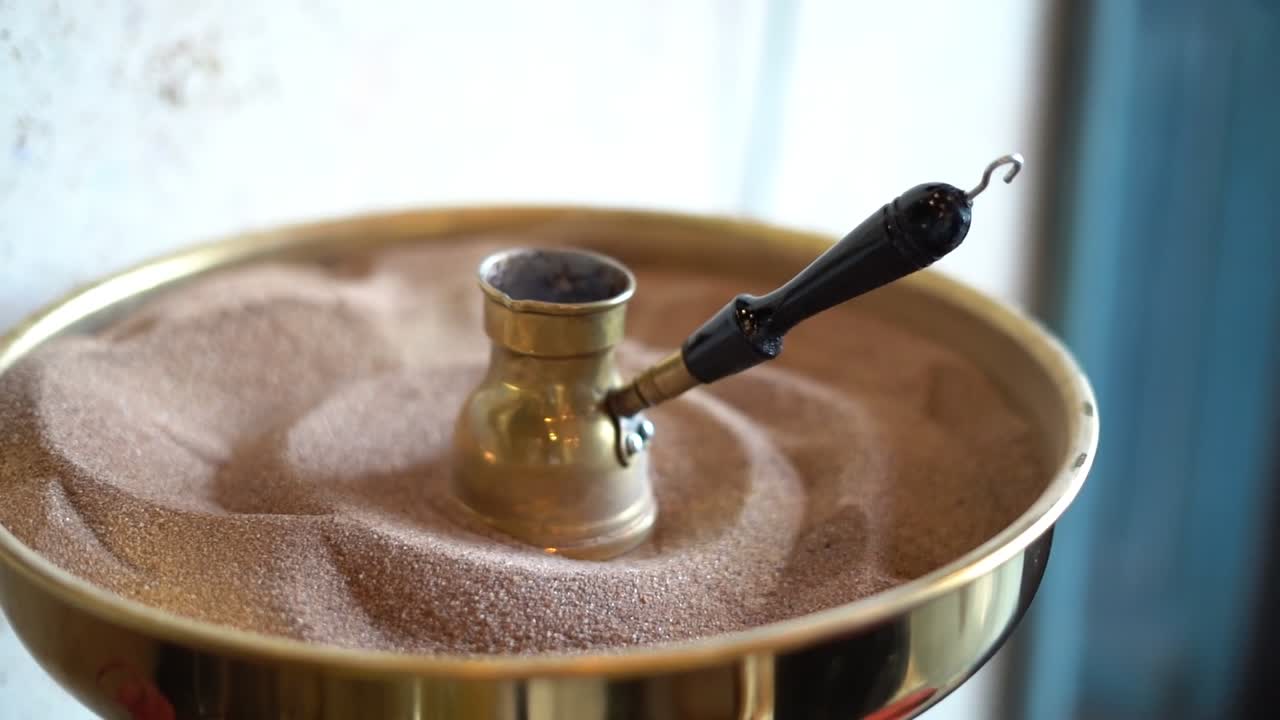 A coffee pot brewing over hot sand, close up shot