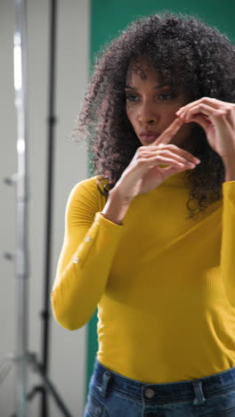 vertical video: woman in yellow sweater posing confidently in studio with curly hair