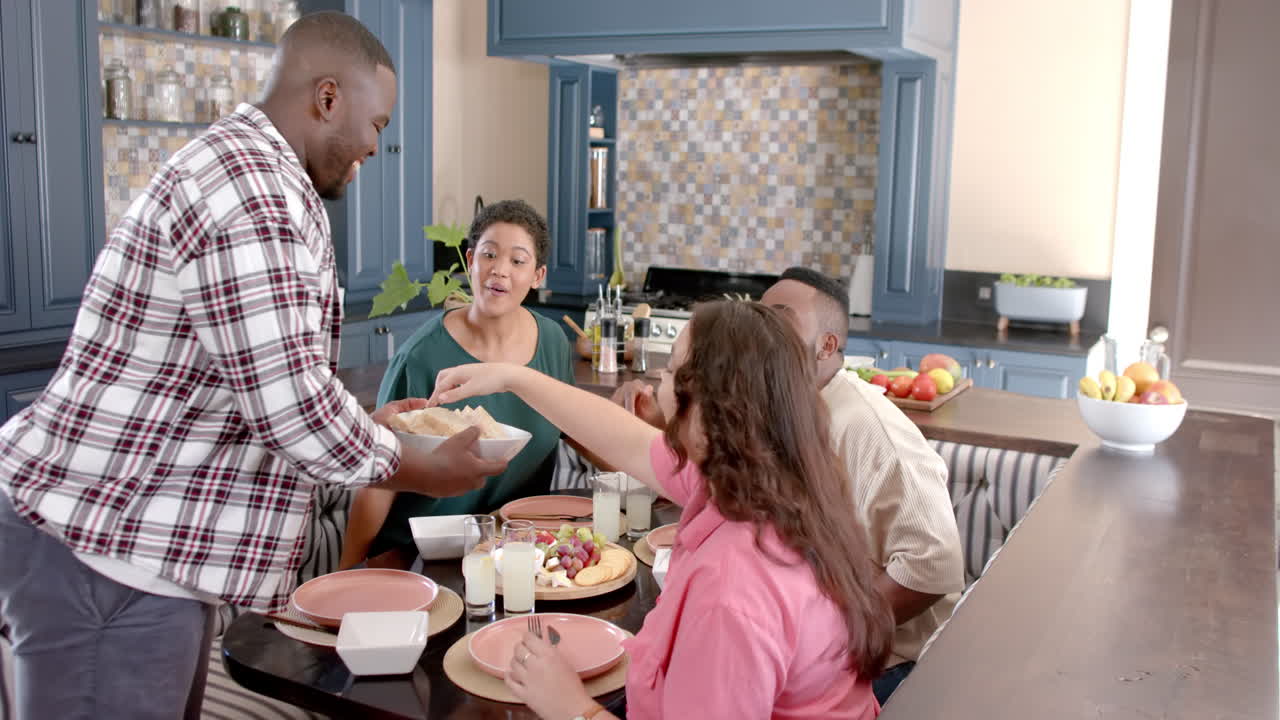 Serving food, African american man sharing meal with diverse friends at dining table in kitchen