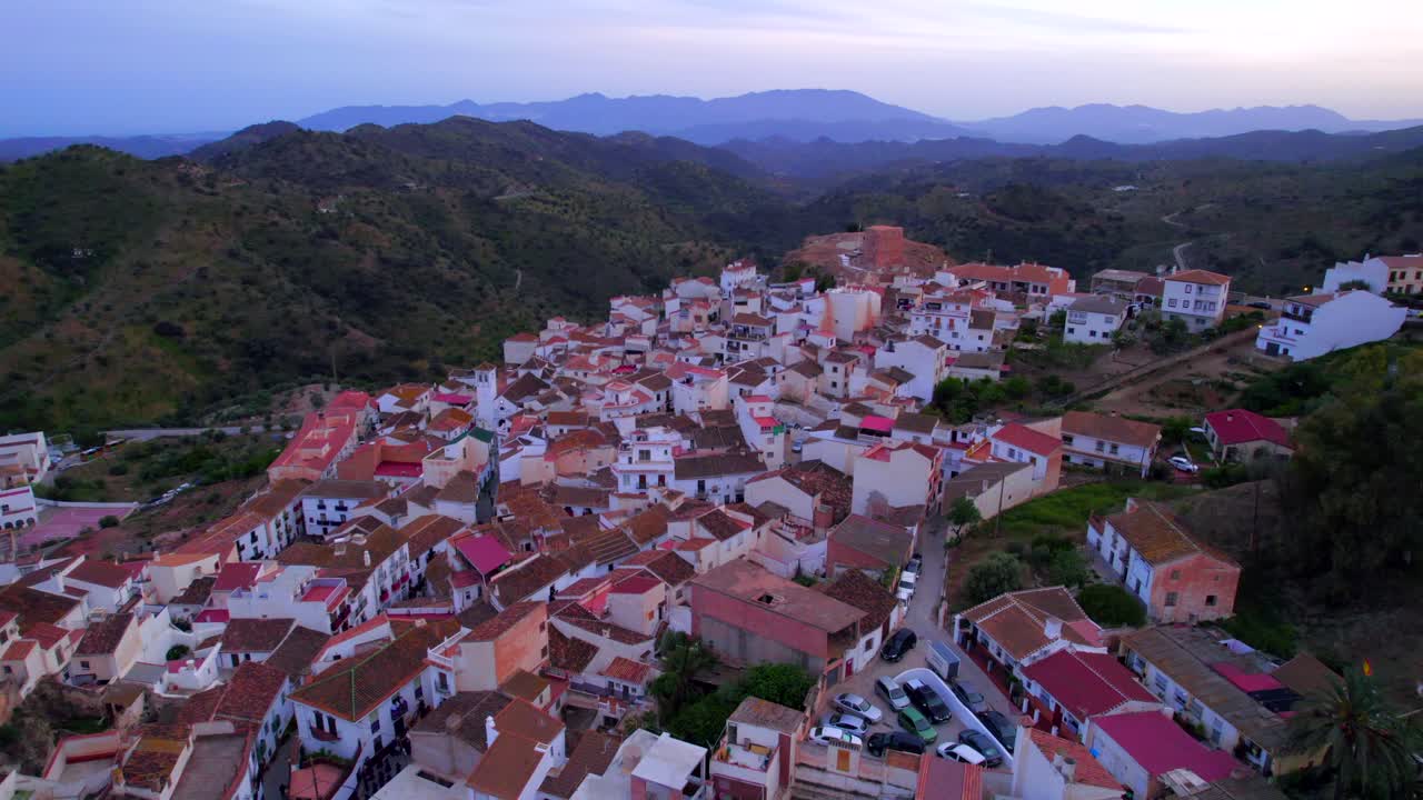 Carrellata aerea in avanti su un pittoresco villaggio tradizionale in cima a una collina a Malaga all'ora blu
