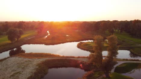 establishing rising drone shot over golf course during sunny sunset in warsaw, poland revealing water ponds, greens and forest