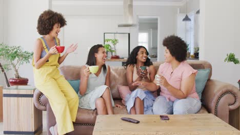 happy diverse female friends sitting on sofa in living room, talking and smiling