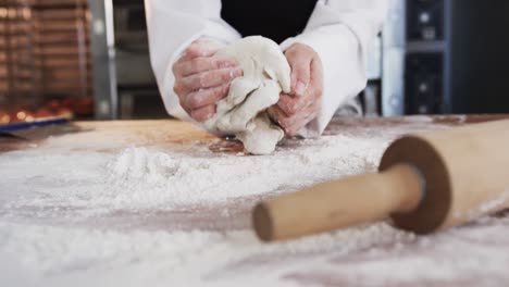 asian female baker working in bakery kitchen, kneading dough on counter in slow motion