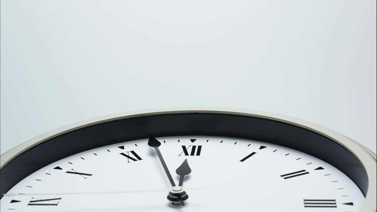 White wall clock short hand points on Roman numerals.