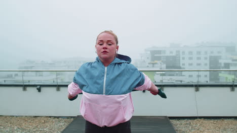 Sporty-girl-in-sportswear-does-yoga-stretching-exercising-using-rubber-band-on-roof-of-house-outdoor