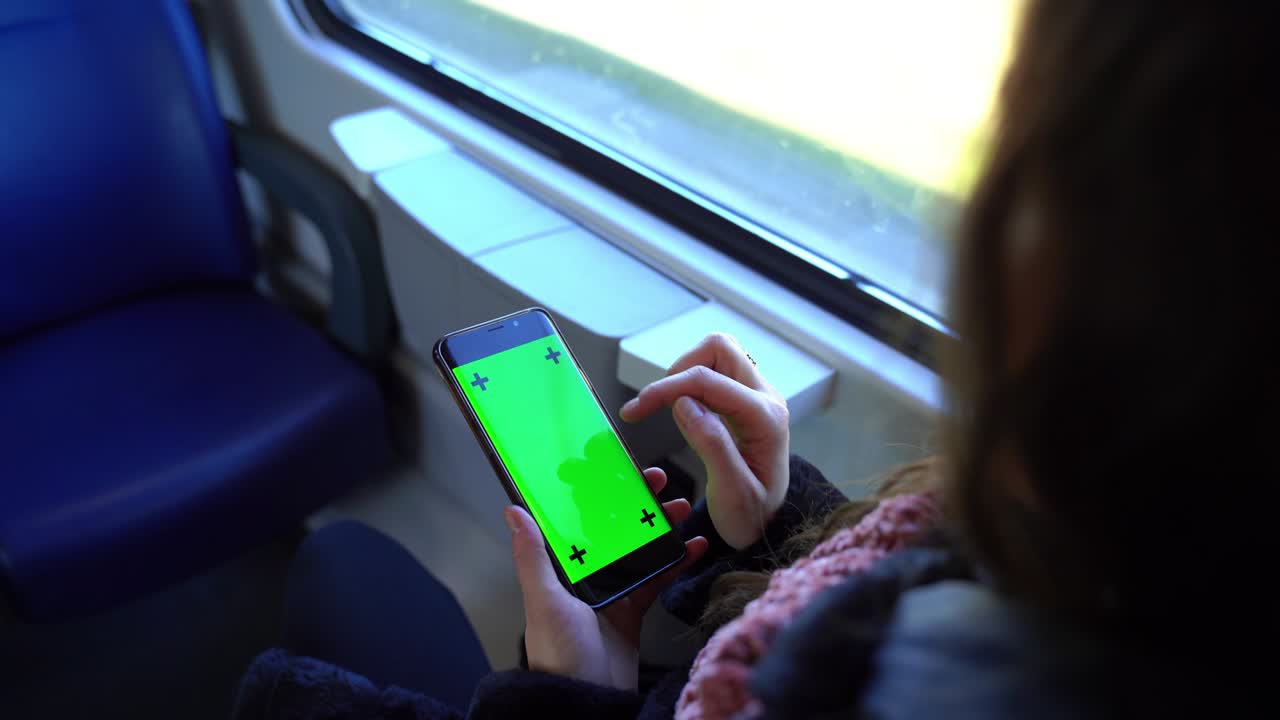 vista superior de la mano de la niña sosteniendo un teléfono inteligente con pantalla verde mientras viaja en tren. pasajera mujer navegando en internet, usando el navegador y sentada cerca de la ventana. teléfono inteligente y destino de viaje