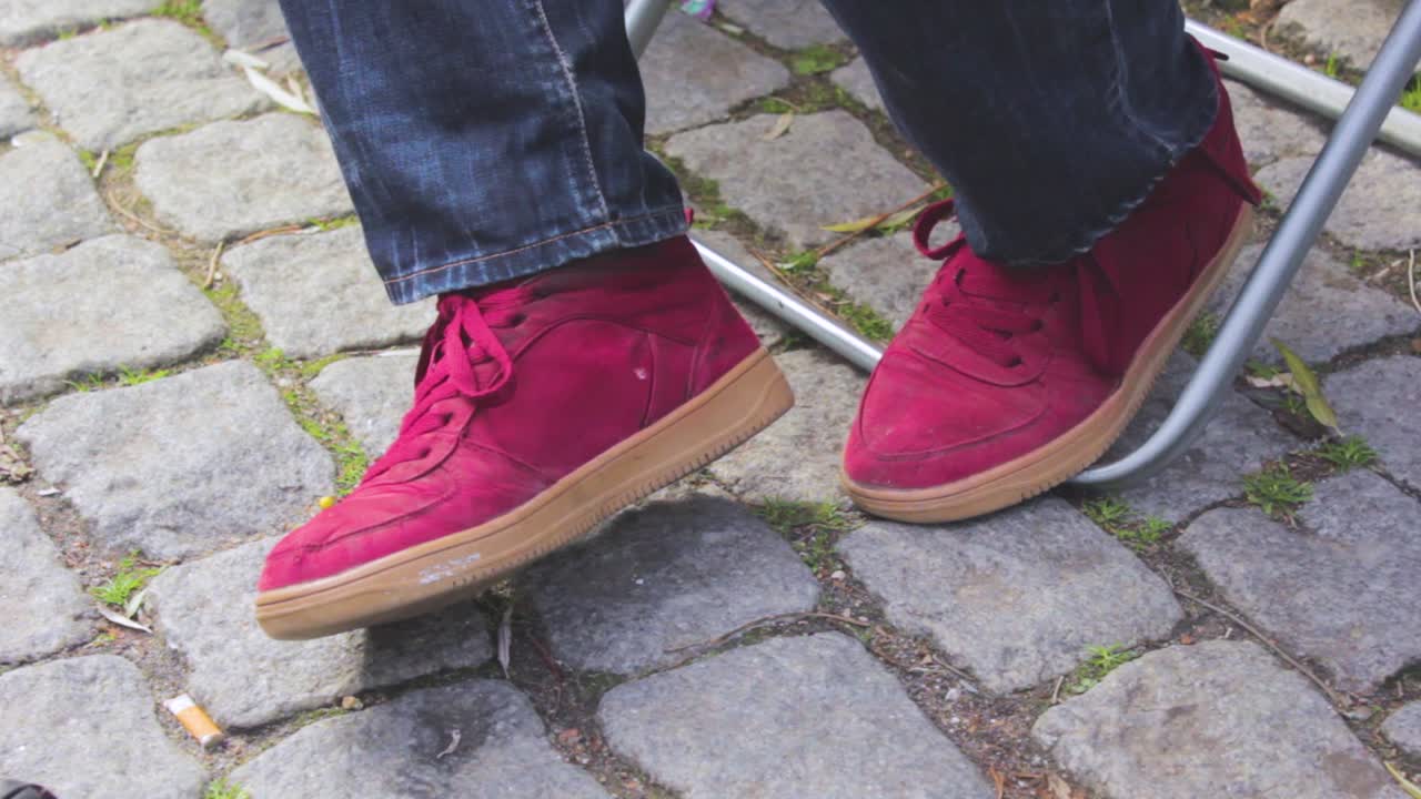 Close up red sports shoes of an adult male sitting on a metal chair in the street with a gray tiles floorMan moving his legs backward Refused and scared with his legs and feel discomfort and insecure