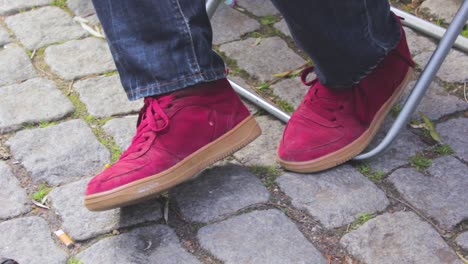 close up red sports shoes of an adult male sitting on a metal chair in the street with a gray tiles floorman moving his legs backward refused and scared with his legs and feel discomfort and insecure