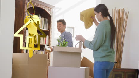 animación de la llave de la casa de oro y el llavero sobre una pareja biracial desempaquetando cajas moviéndose a una nueva casa