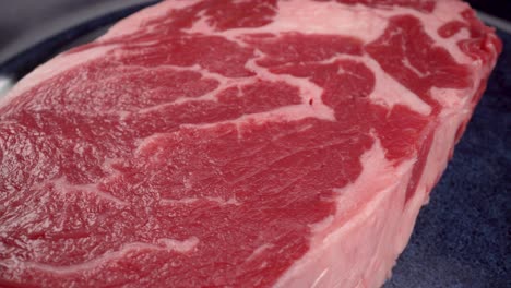 entrecôte ribeye steak close up, rotation, 4k macro view of red meat with fat on blue plate, beef