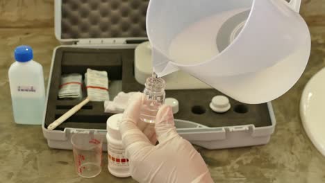 con los guantes de mano verter líquido transparente en la botella de muestra de vidrio, cerrar