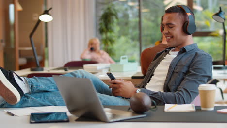 young businessman with feet on desk in office listens to music on wireless headphones