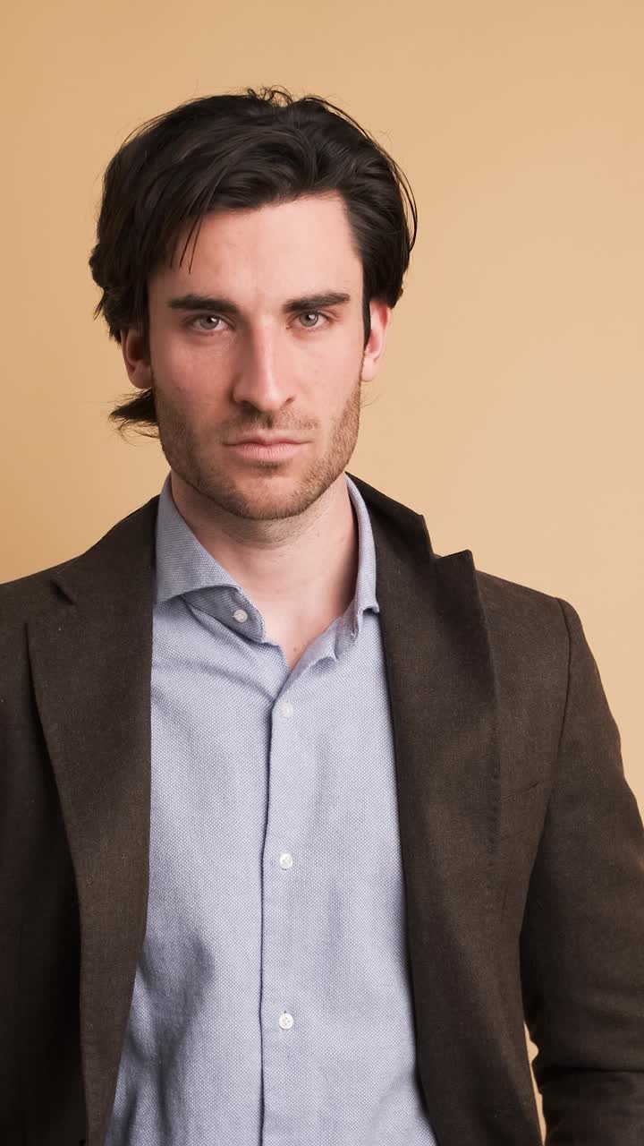 Serious businessman in blazer looking at camera in blue studio