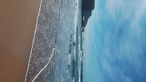 Zambujeira-do-Mar-over-the-sea-shore-with-ocean-waves,-cliffs-and-sand-dunes-covered-by-green-vegetation-red-leaves-of-sour-fig,-sunny-day,-clear-blue-sky