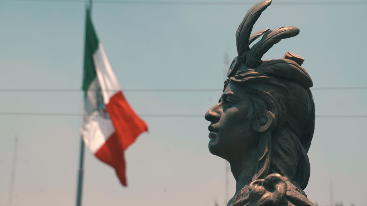 Mexican flag flying high on a pole in front of the Cuauhtémoc statue, symbolizing national pride